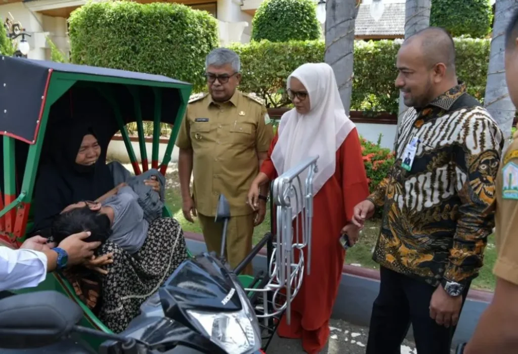 Foto: Pj Gubernur Aceh Bustami bersama istri Mellani Subarni, didampingi Plt Direktur Utama Bank Aceh Syariah, Fadhil Ilyas, menyerahkan bantuan satu unit becak untuk Abdul Azis untuk operasional pengobatan anaknya Muhammad Ramadhan yang menderita sakit lumpuh sejak lahir, di halaman Pendopo Gubernur, Senin, (10/6/2024).